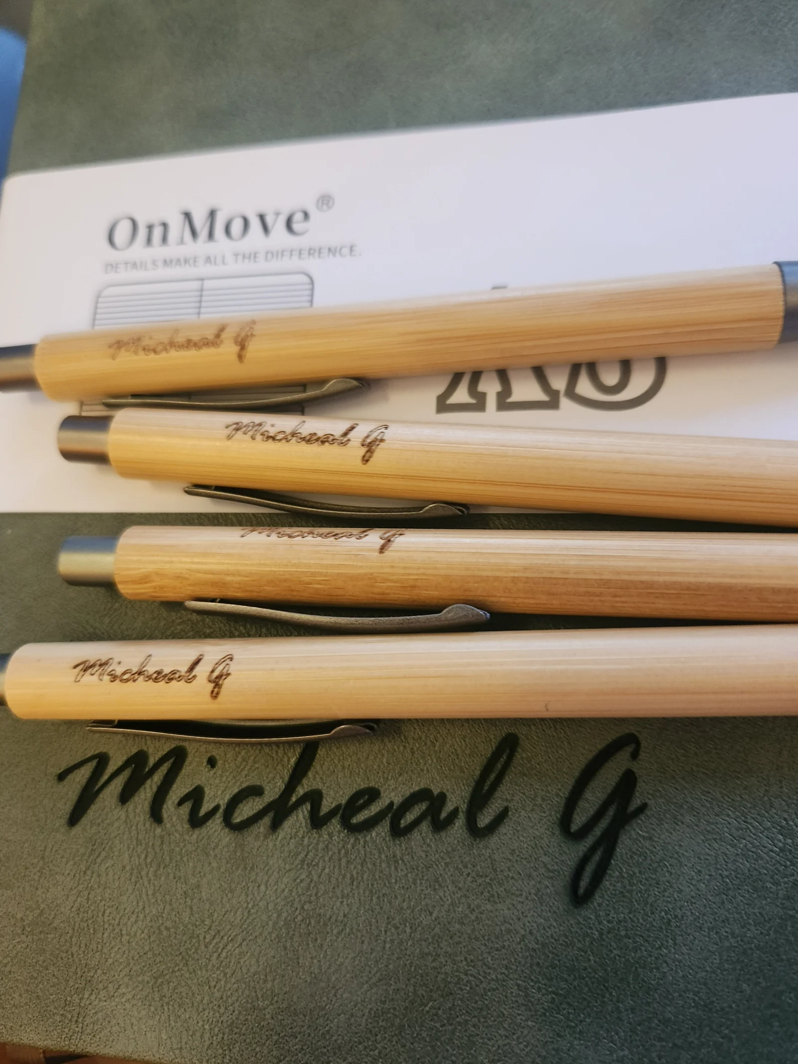 Close-up of engraved wooden pens with 'Micheal G' names, and cursive 'Micheal G' text on the journal.