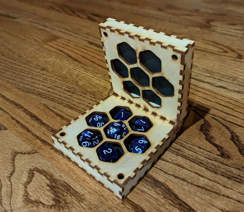 A wooden box with a honeycomb pattern and blue translucent dice inside, set on a wooden surface.