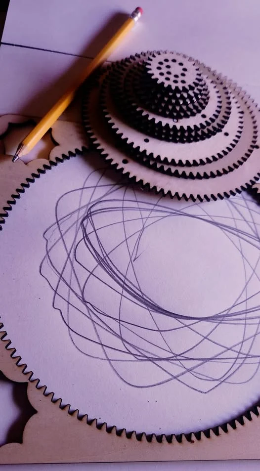 A wooden gear with a pencil on top, layered over circular sketches on paper, suggesting a design process.