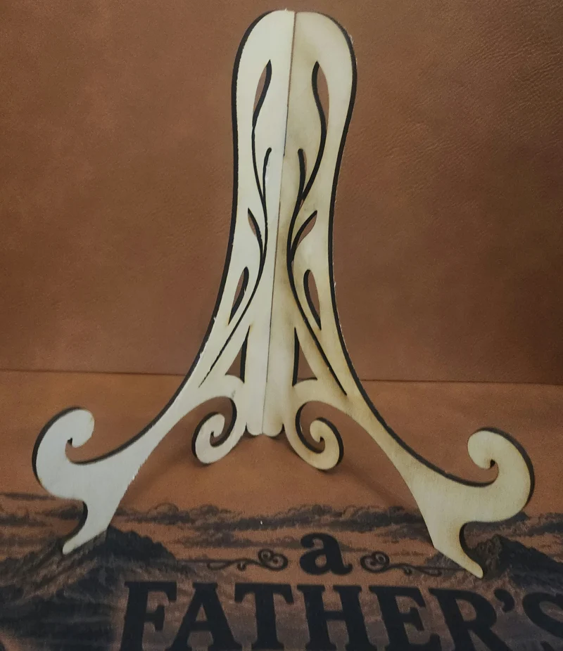 A white wooden cutout with swirling patterns and curves, placed against a brown textured background with text partially visible.