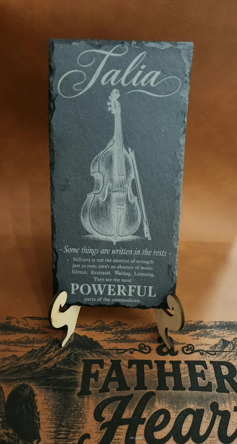 Personalized Talia double bass slate displayed on a wooden stand, engraved with an inspirational message comparing stillness in life to rests in music.