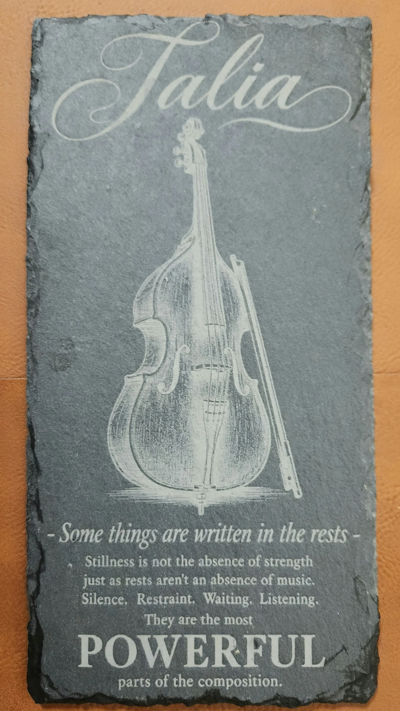 Close-up of a personalized engraved black slate for Talia featuring a double bass and bow with a message about the power of stillness, listening and rests in music.