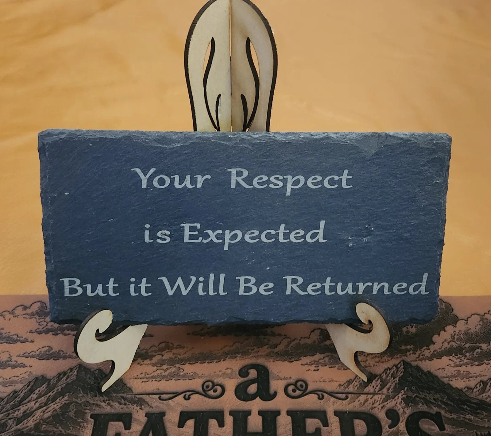 A blue slate sign with white text that reads, 'Your Respect is Expected But it Will Be Returned,' supported by a decorative leaf-like element. The background includes a muted earth-toned layered artwork with a faint mountain landscape.