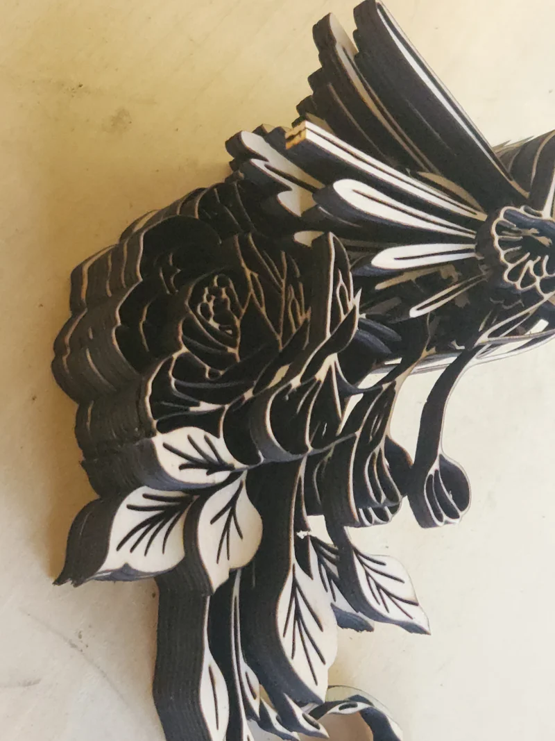 Layered laser-cut wooden artwork of a hummingbird flying beside a large rose with detailed leaves and flowers, created in memory of the artist's late mother and her love of hummingbirds Closeup of stacks