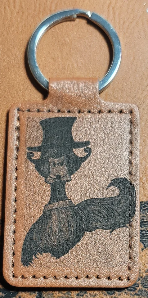 Photograph of a portrait tan stitched keychain featuring a front-facing duck with a tall top hat and an oversized curled mustache.