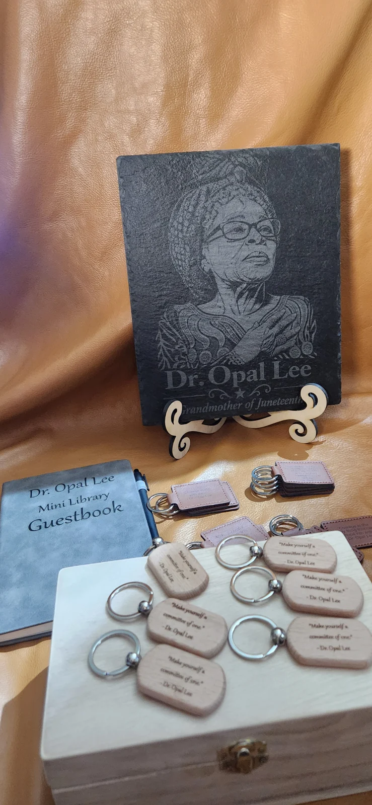 Display honoring Dr. Opal Lee featuring her engraved portrait on black slate, an open Little Free Library guestbook, and leather keychains engraved with her quotations.