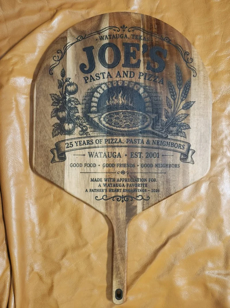 Close-up of a custom engraved wooden pizza peel honoring Joe's Pasta & Pizza in Watauga, Texas, featuring a brick pizza oven, tomatoes, wheat and a 25 years of pizza, pasta and neighbors anniversary design.