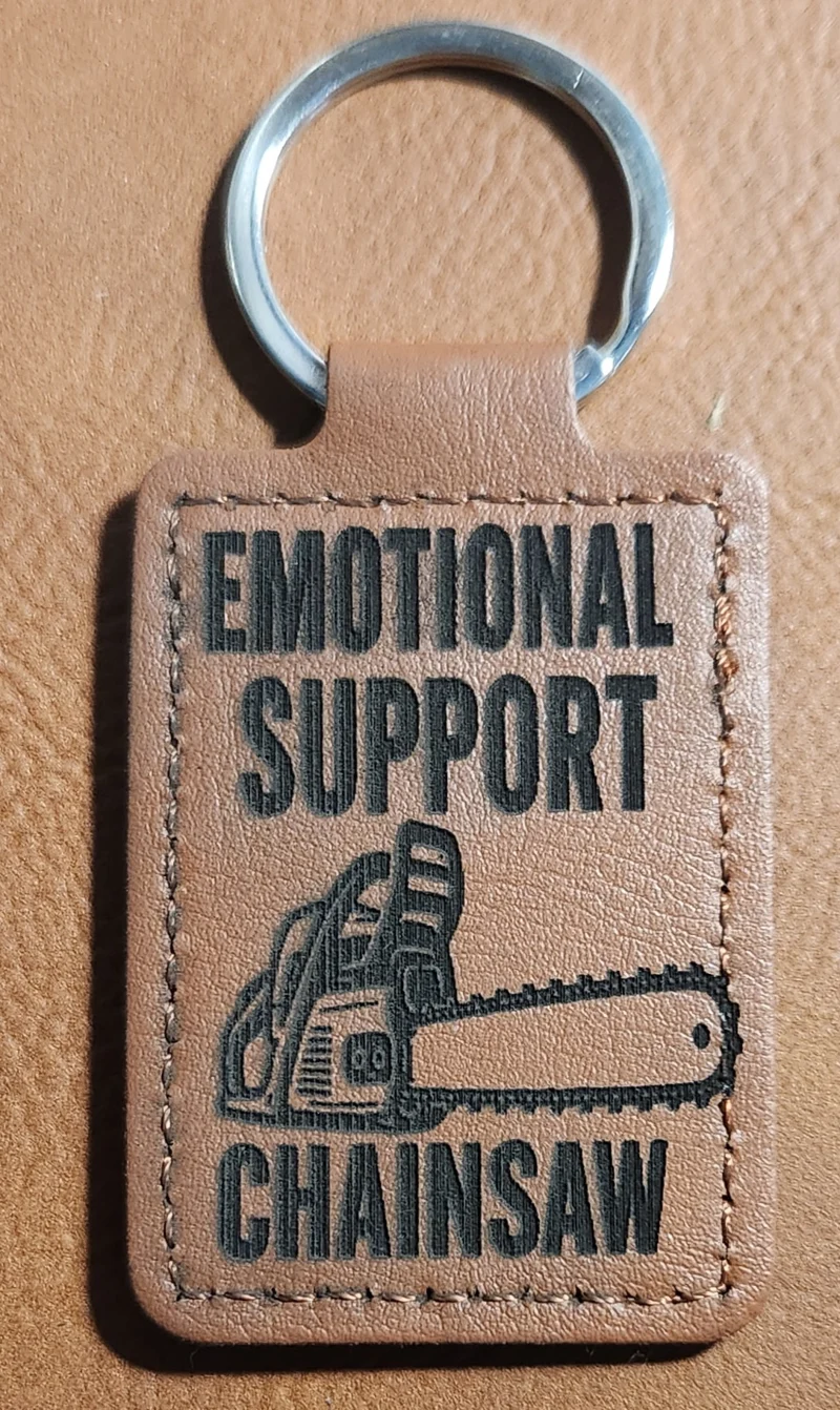 Tan stitched portrait keychain with a chainsaw illustration and the words EMOTIONAL SUPPORT CHAINSAW.